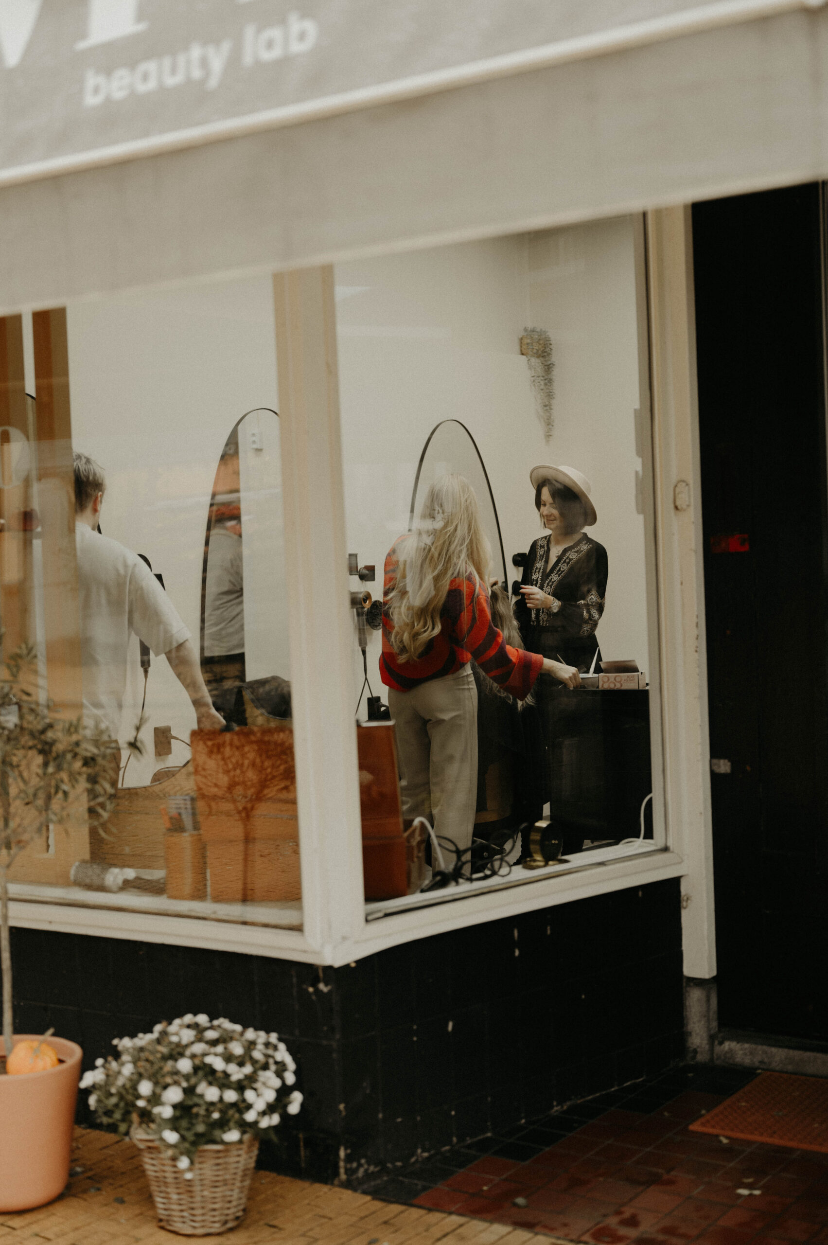 Een blik door het raam van 'beauty lab' onthult een hair weave specialist, Noel, die aan het werk is in de salon.</p>
<p>