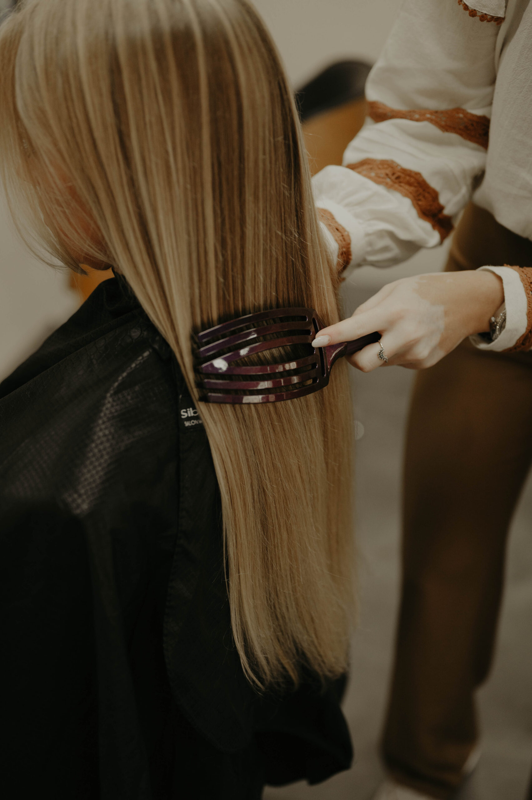 Een stylist gebruikt een Olivia Garden borstel om het lange, blonde haar van een klant in de kapsalon te kammen.